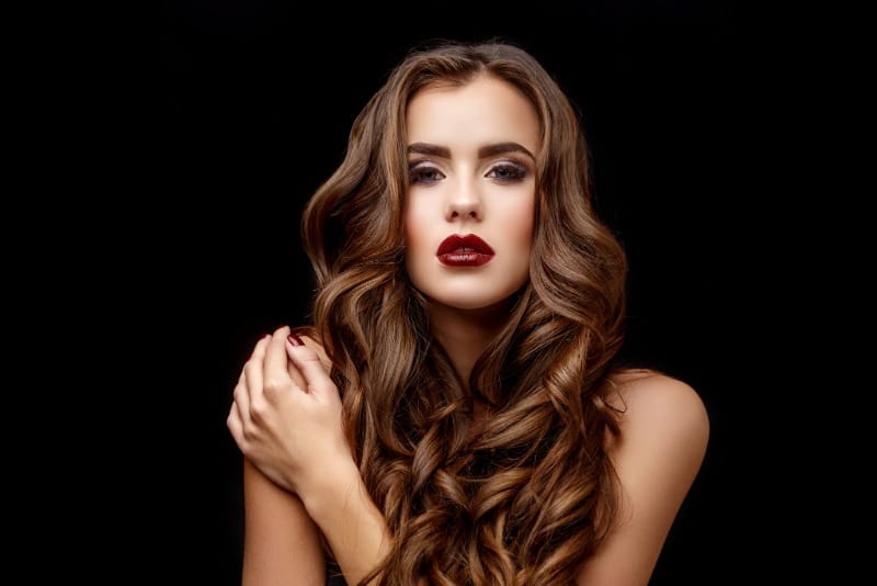 Mujer con cabello castaño largo y ondulado sobre fondo negro