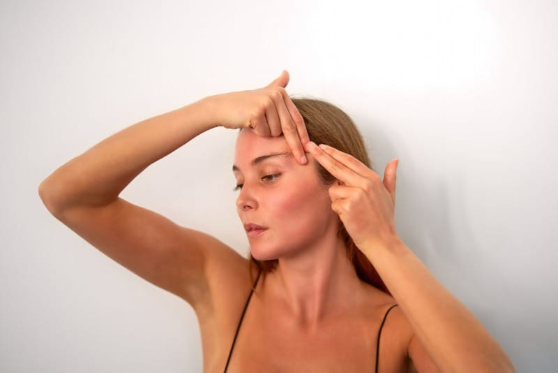 Mujer con el cabello recogido y las manos sobre la frente y la sien