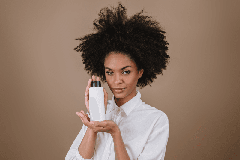 Mujer con cabello rizado que presenta un frasco blanco con tapa negra
