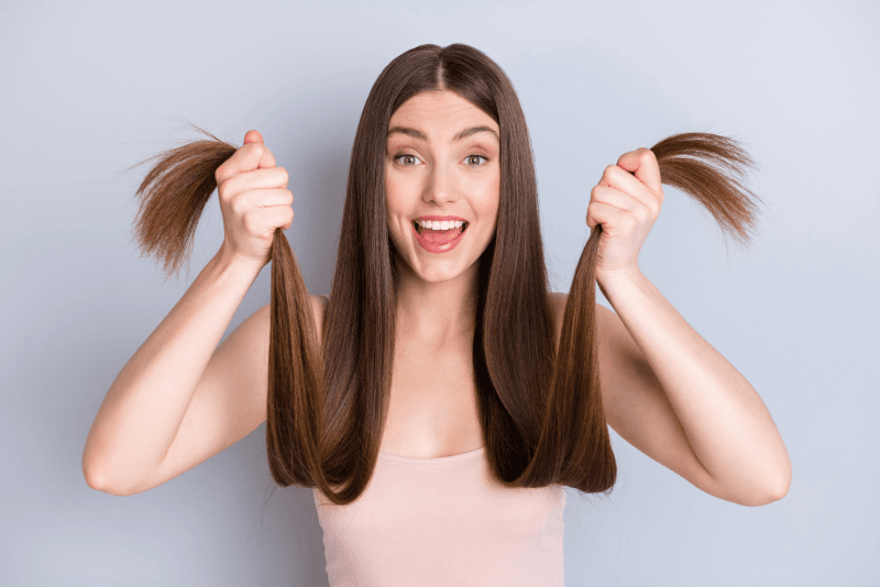 Mujer con cabello castaño liso que sostiene las puntas con ambas manos