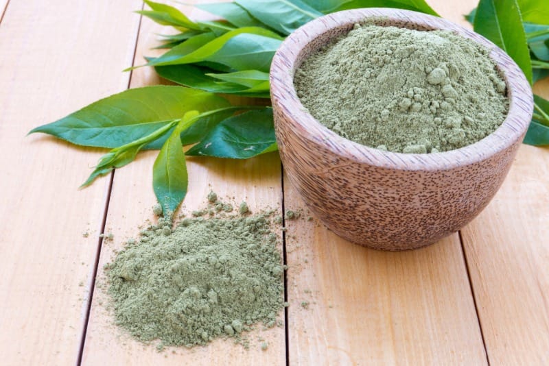 Polvo vegetal verde en un cuenco de madera junto a hojas sobre una mesa